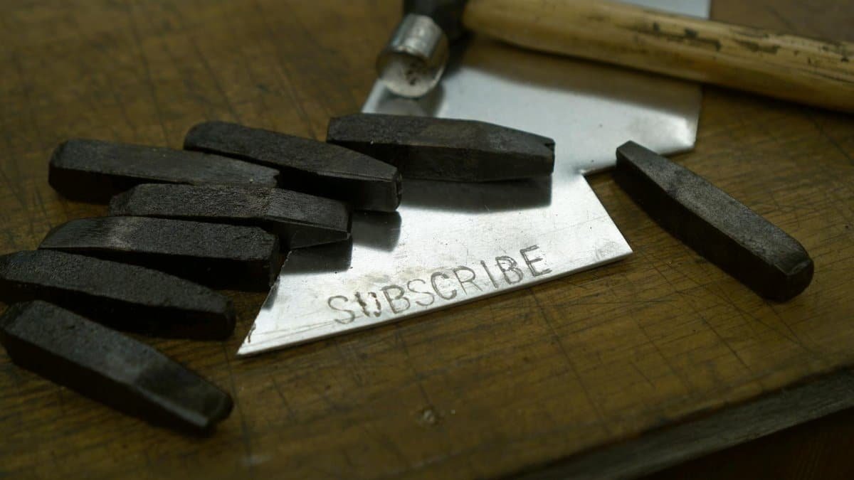 Vintage letter stamps and hammer on wood surface with 'SUBSCRIBE' on metal sheet.