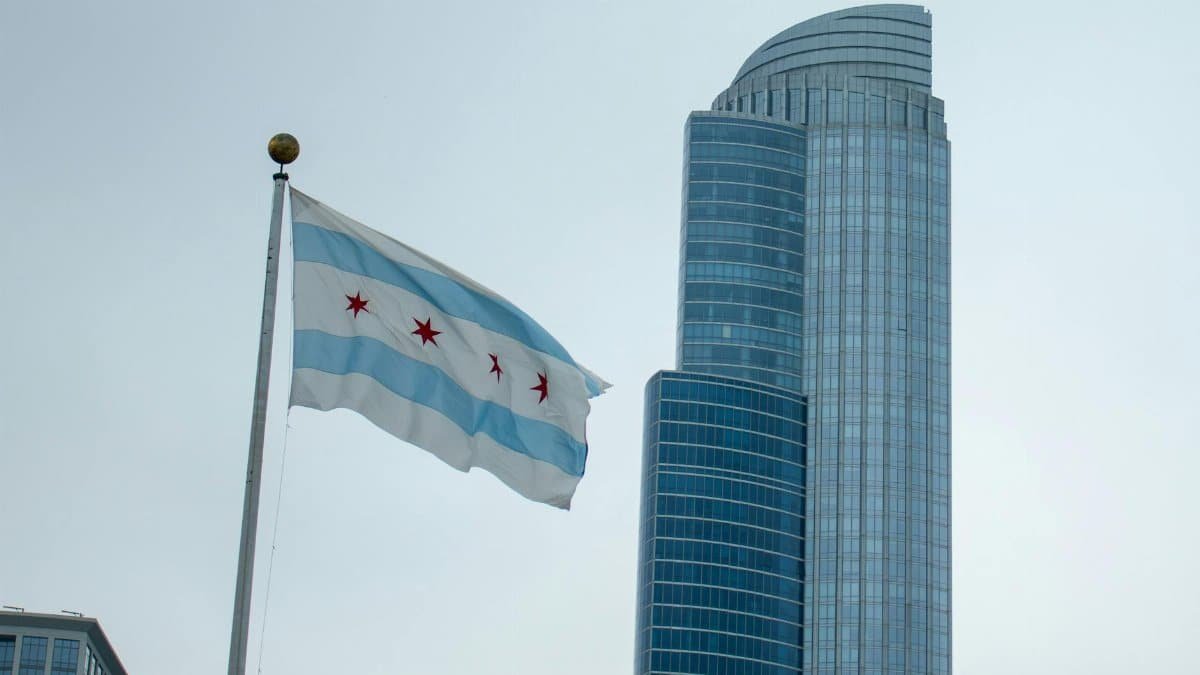 Chicago flag waving in front of a modern skyscraper on a clear day.