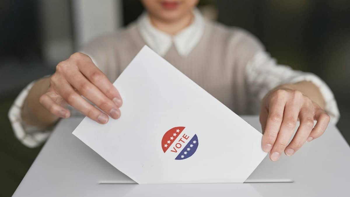 A person casting a vote by placing a ballot into a ballot box, symbolizing democratic participation.