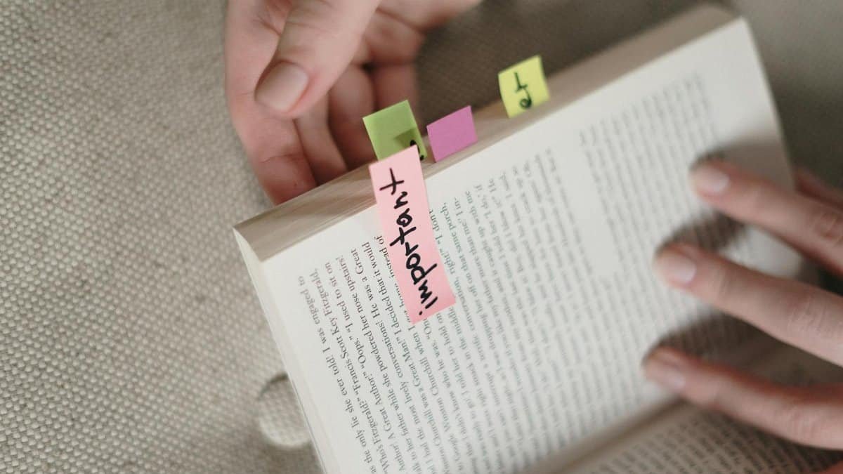 Hands holding a book with colorful sticky notes marking important pages.