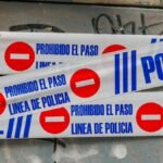 Police tape with 'Prohibido El Paso' against graffiti-covered wall. Crime scene concept.