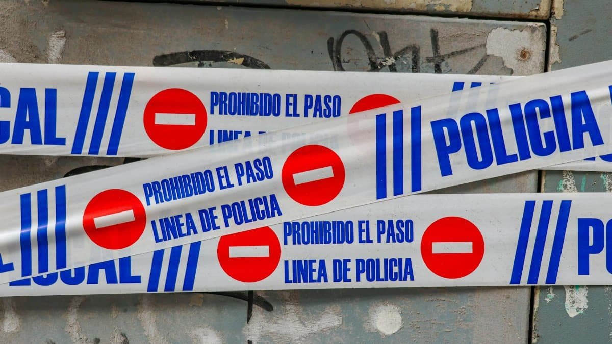 Police tape with 'Prohibido El Paso' against graffiti-covered wall. Crime scene concept.