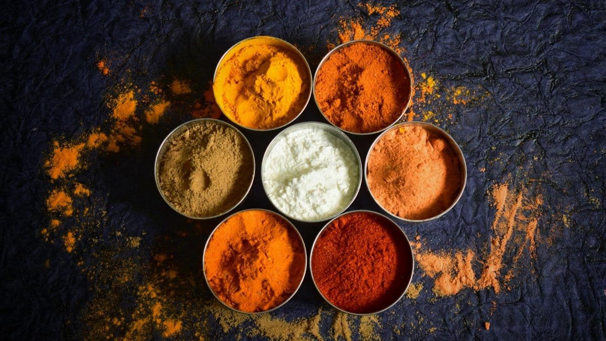 Colorful Indian spices in bowls on a textured dark background for culinary concepts.
