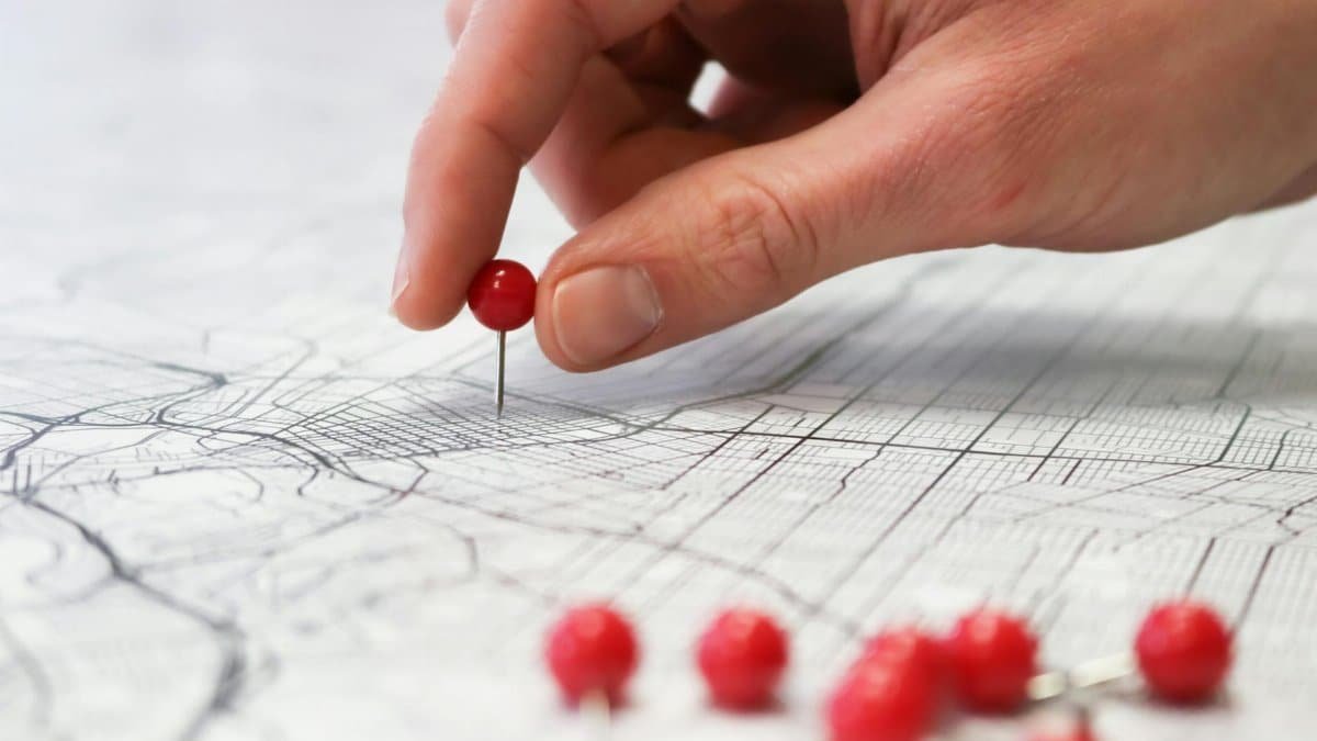 Close-up of a hand placing a red pin on a map indicating geographic location pinning.
