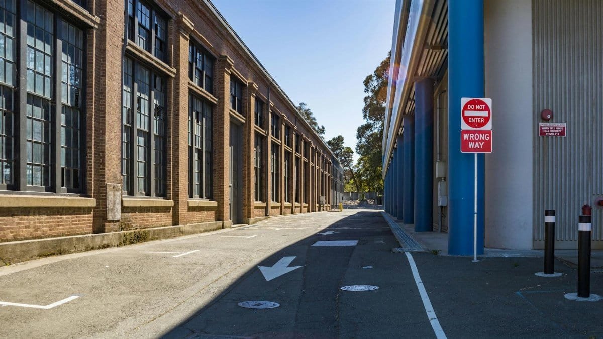 Exterior of a large industrial building with 'Do Not Enter' and 'Wrong Way' signs on a sunny day.