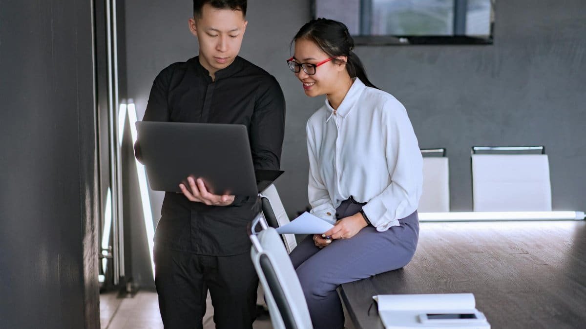 Two professionals collaborating in an office with a laptop, discussing documents and ideas.
