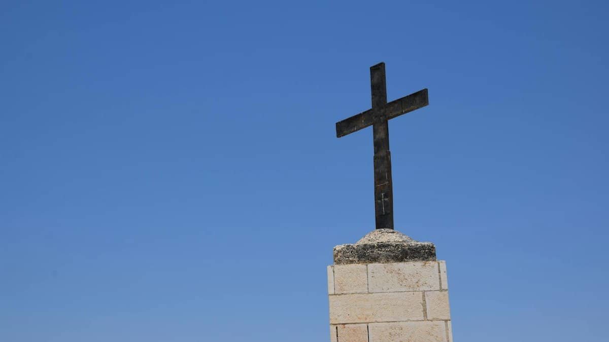 A solitary cross on a stone base stands tall against a vibrant blue sky, symbolizing faith and spirituality.