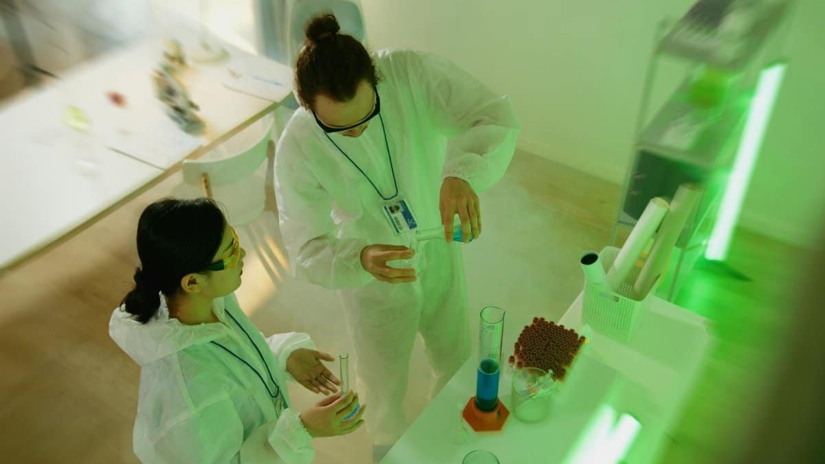 Two scientists in protective clothing conducting a laboratory experiment with beakers.