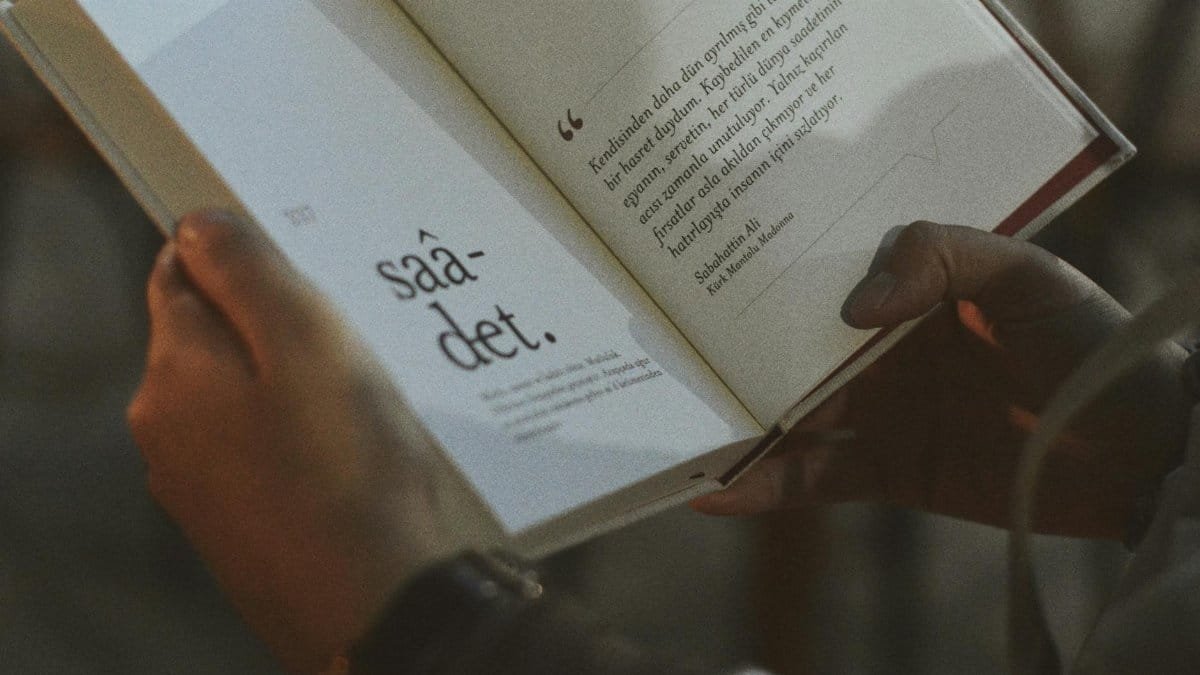 Person holding and reading an open book with visible text.
