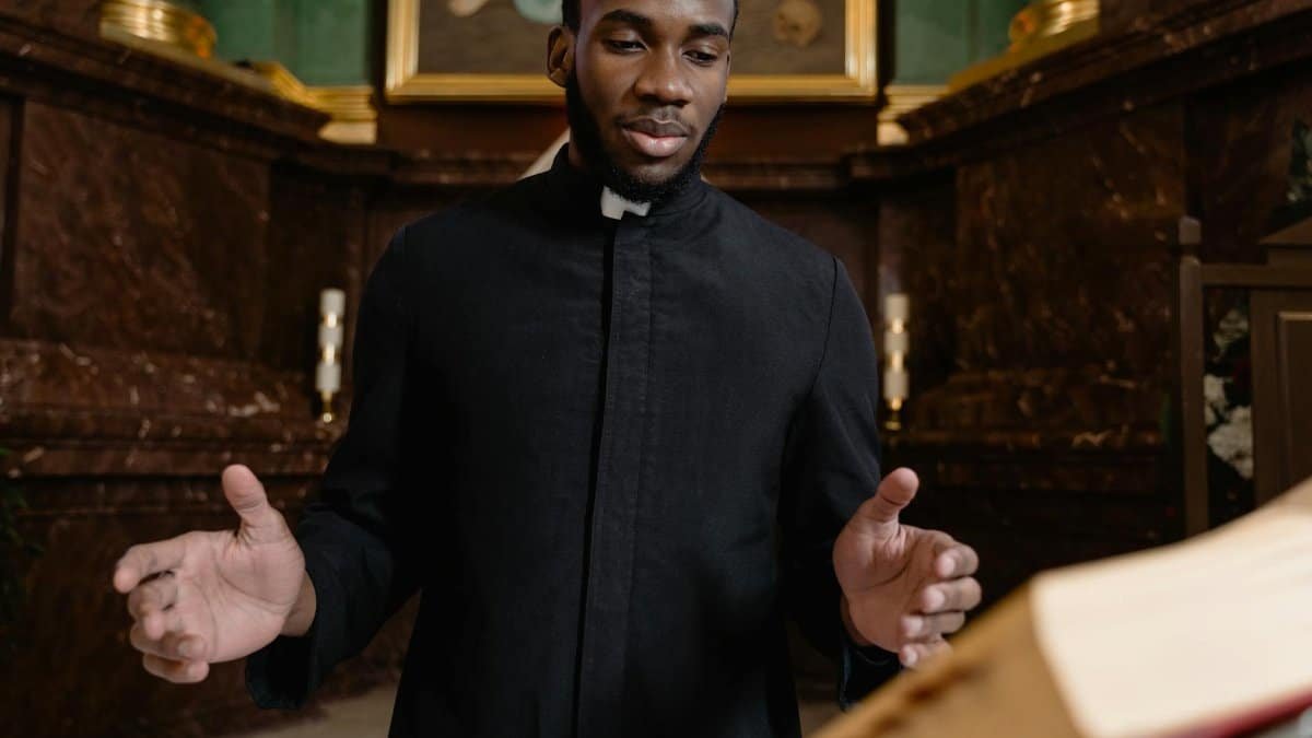 Priest in black vestment conducting a ceremony at a church altar with open book.
