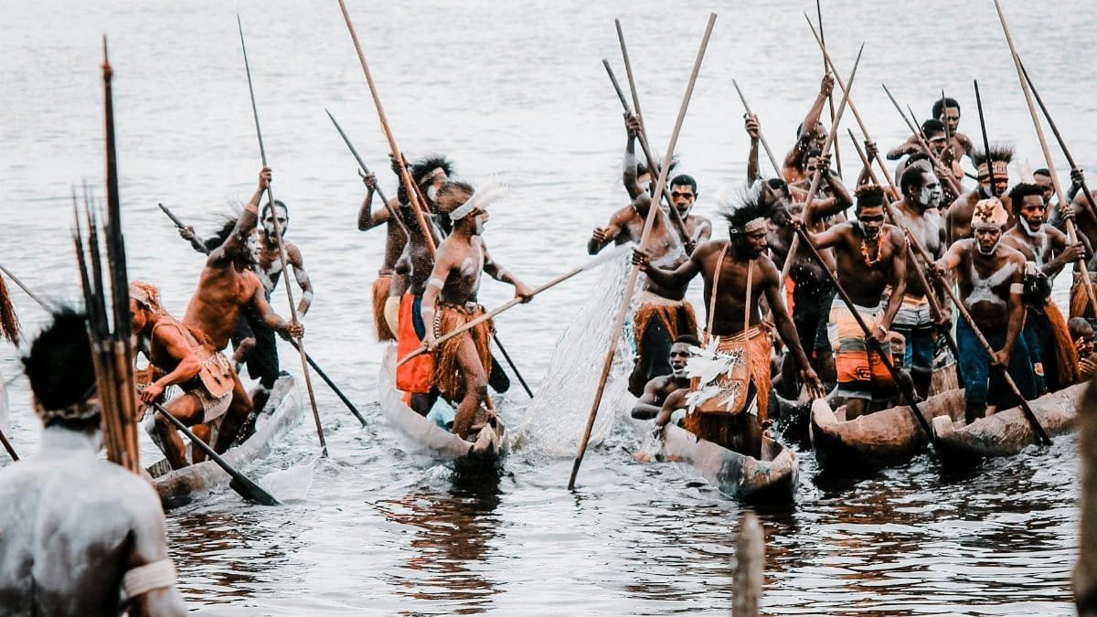 Indigenous tribes in Papua, Indonesia, engaged in a traditional canoe race on a serene water body.
