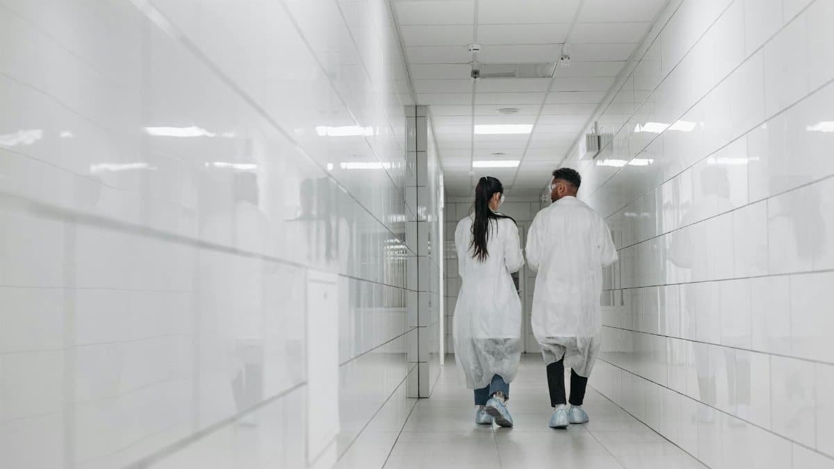 Two scientists in lab coats walk down a bright, tiled hallway, showcasing modern research environment.