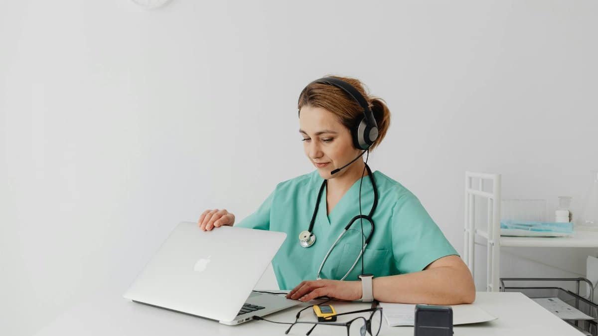 A female medical professional using a laptop and headphones in a modern office setting.