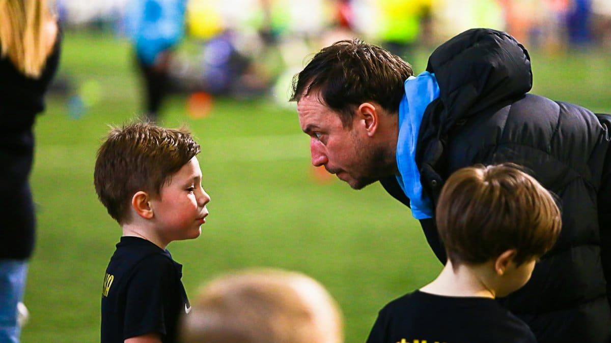 A soccer coach gives guidance to young boys during an indoor soccer training session.