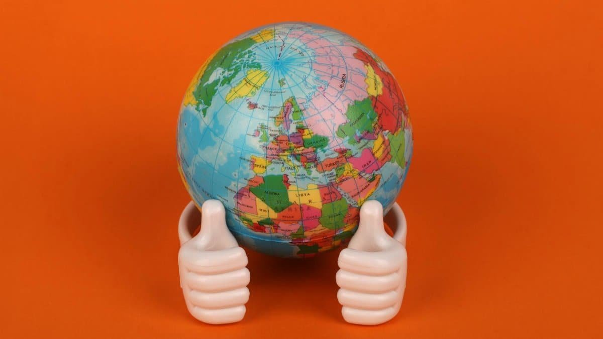 Vibrant globe model with thumbs-up figurines on orange background, symbolizing global positivity.