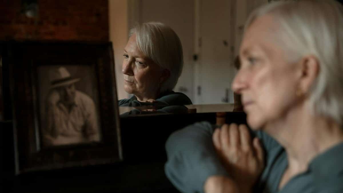 Elderly woman reflects on memories, gazing at a framed photo, deep in thought.