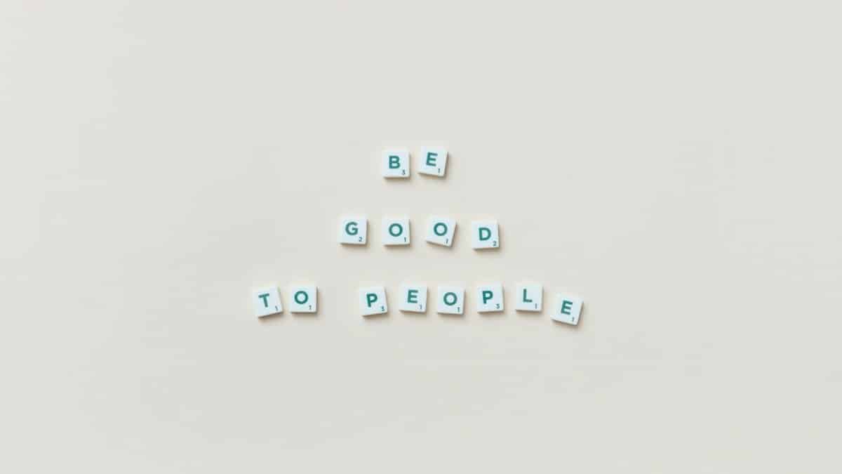 Scrabble tiles arranged with the inspirational quote 'Be Good to People' on a neutral background.