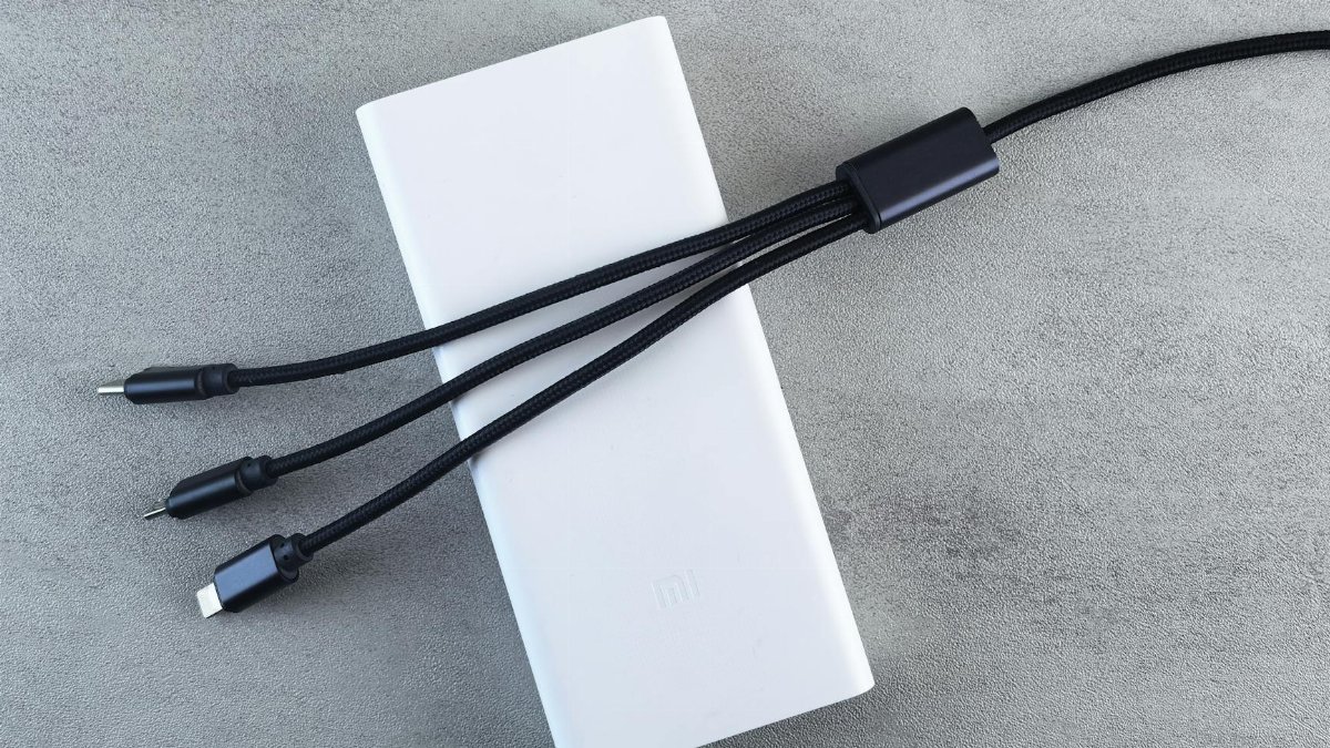 A sleek white power bank with a black multi-connector cable laid on a textured grey surface, emphasizing modern technology.