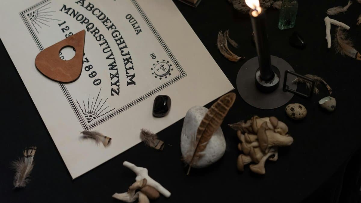 Dark, mystical setup featuring an Ouija board with candles and occult symbols for spiritual practice.