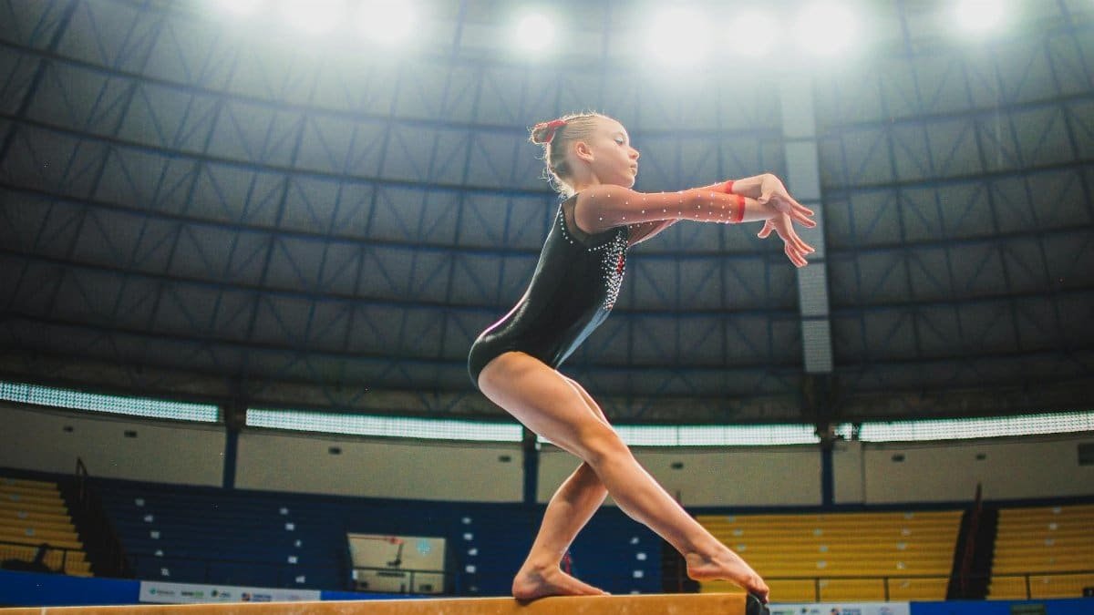 A young gymnast performing a routine on the balance beam indoors during a competition.