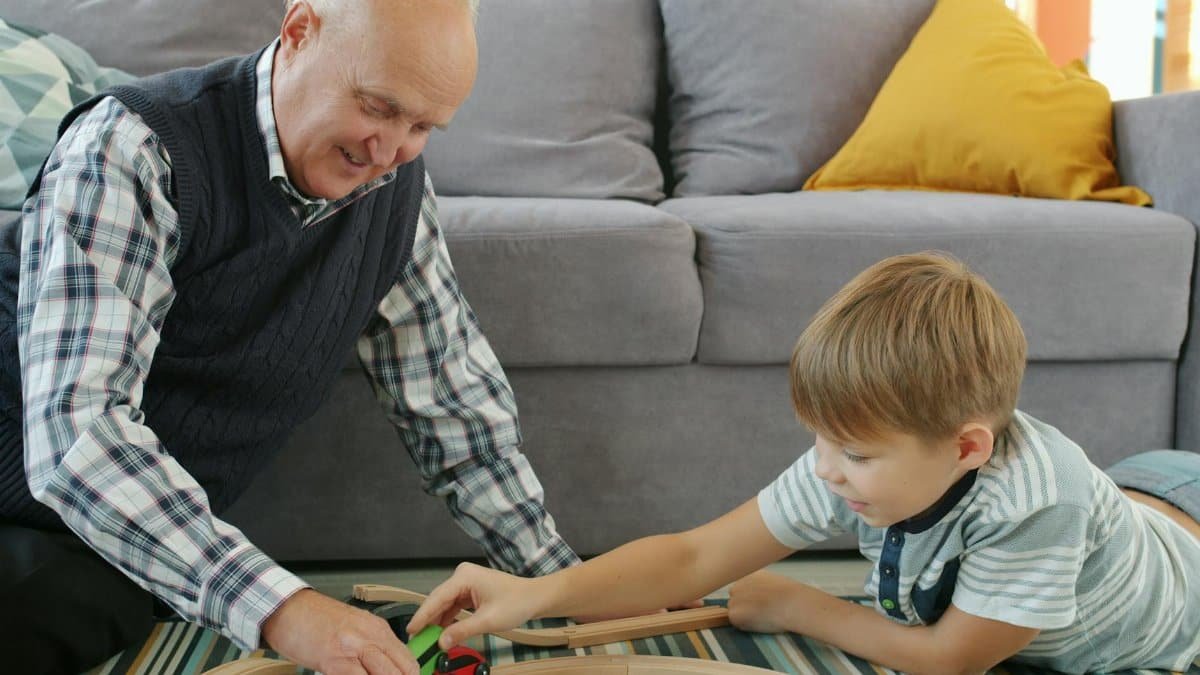 A joyful moment of grandfather playing with grandson on the floor with a toy train.