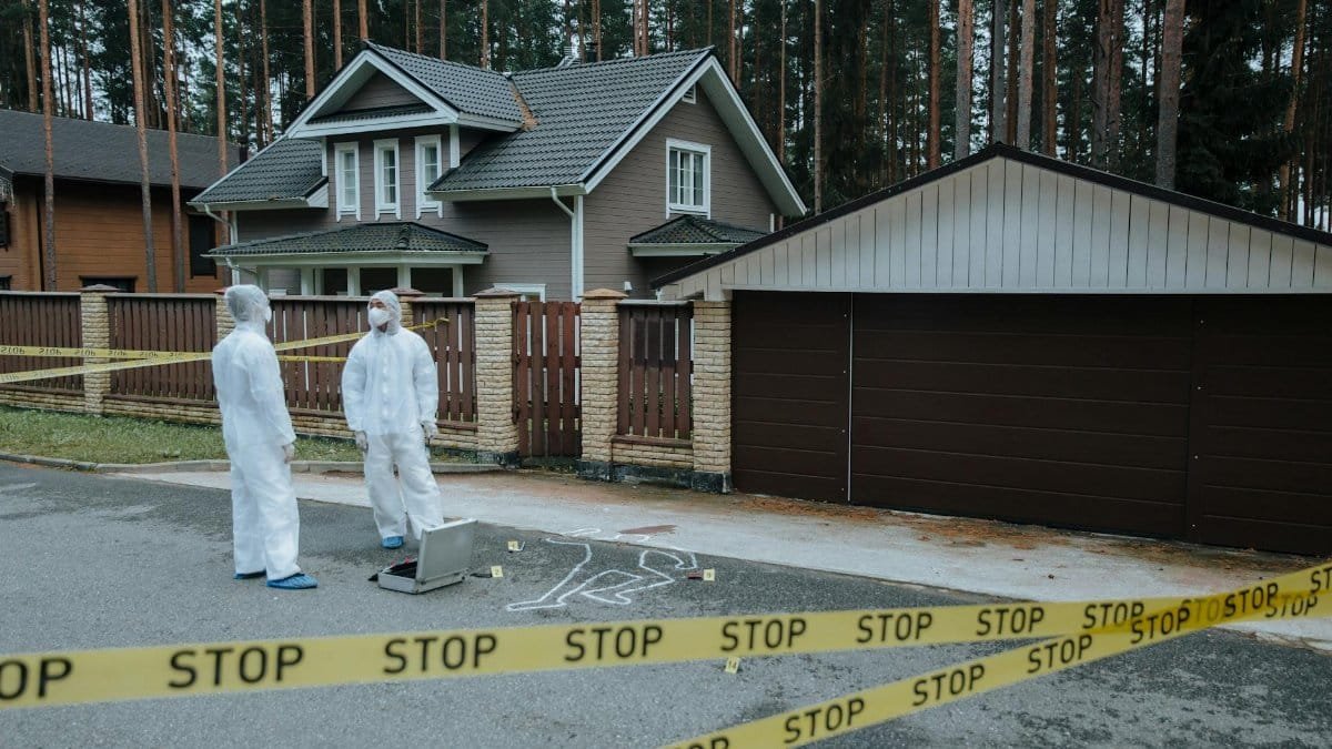 Crime scene investigators in protective suits examining evidence at a suburban house with yellow tape.