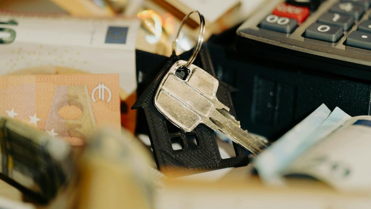 House keys rest on a keychain with euro banknotes and calculator, symbolizing real estate investment.