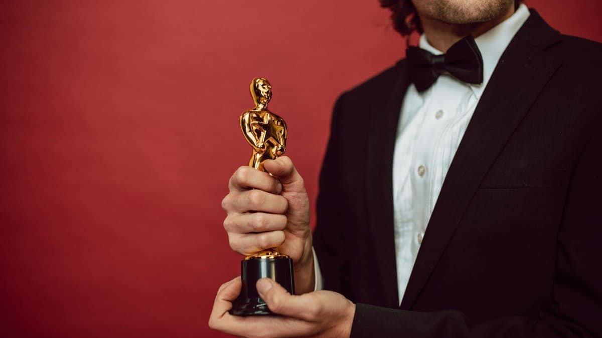 Elegant man in tuxedo holding a gold trophy against a red background, celebrating an achievement.