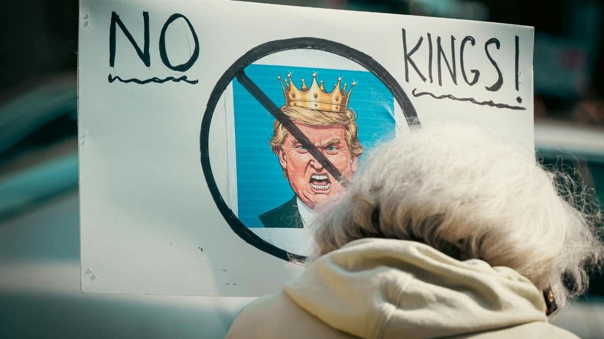 A protest sign reading 'No Kings' depicts resistance against monarchy with a satirical image.