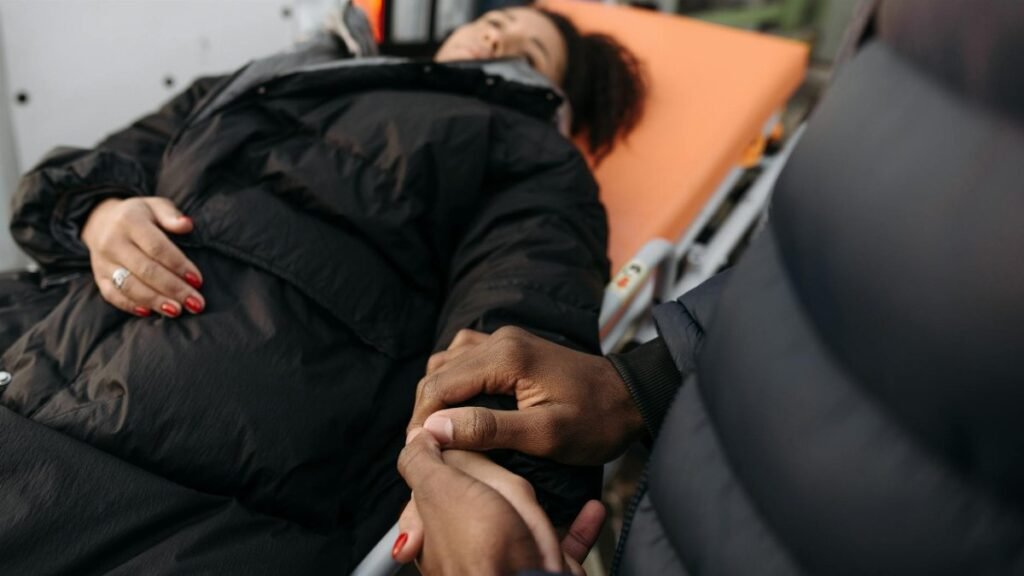 A woman lying on a stretcher as a comforting hand holds hers. Indoor medical care scene.