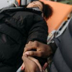 A woman lying on a stretcher as a comforting hand holds hers. Indoor medical care scene.