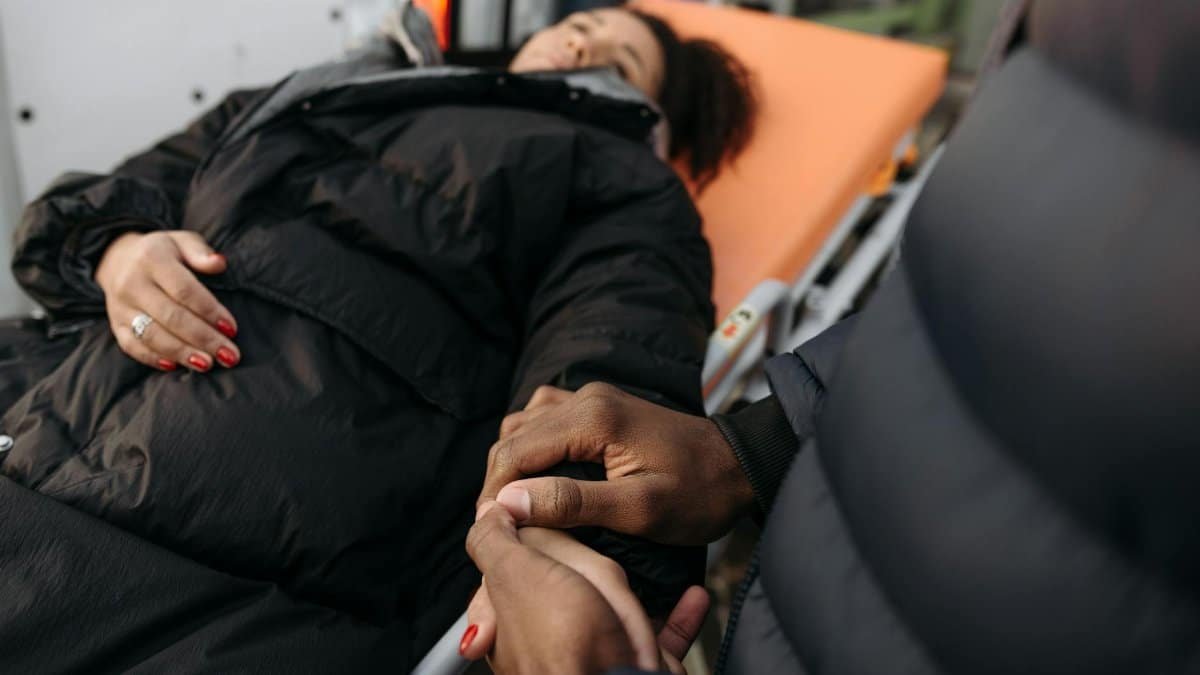 A woman lying on a stretcher as a comforting hand holds hers. Indoor medical care scene.