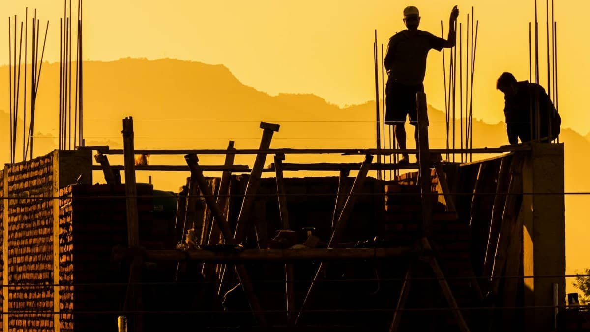 Silhouette of construction workers on a building site at sunset, showcasing urban development.