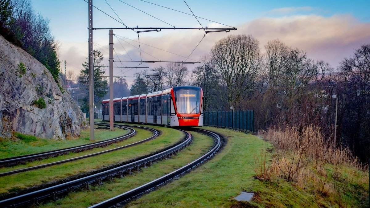 A modern tram navigating through a scenic rail track curve surrounded by nature.