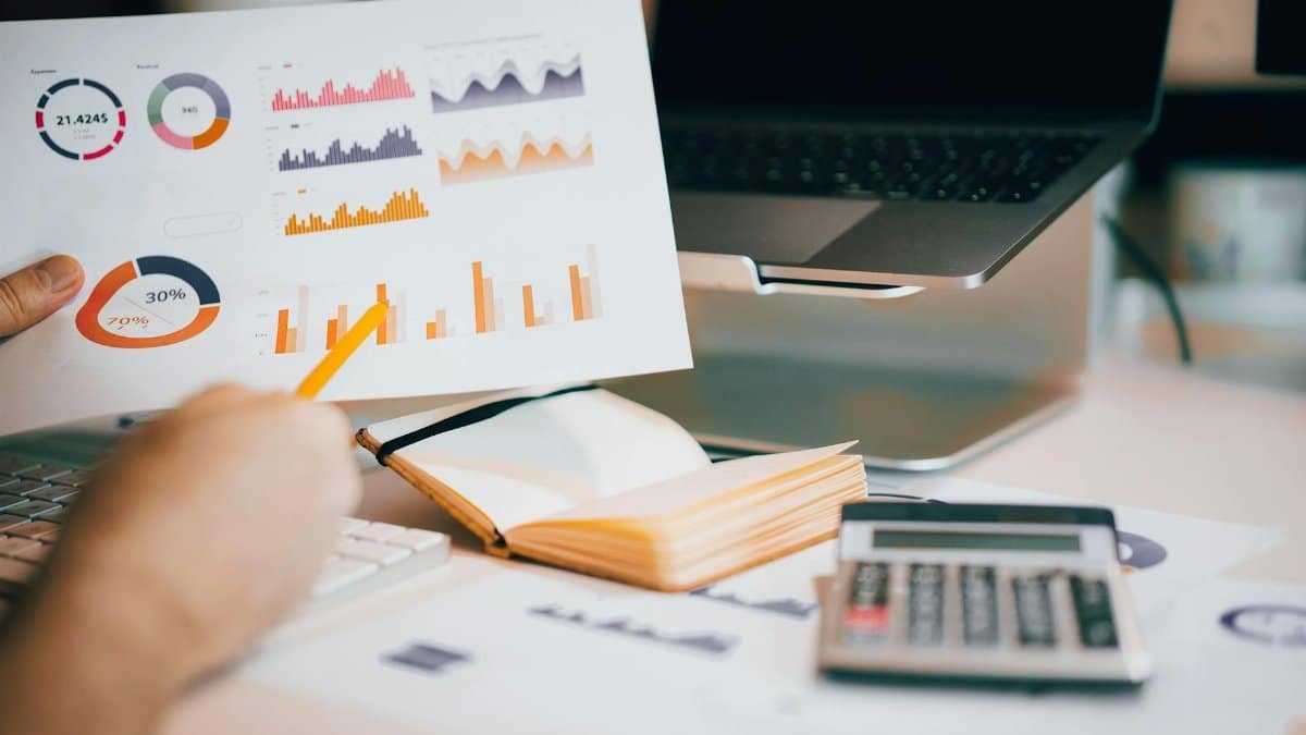 Close-up of hands analyzing financial data with charts, laptop, and calculator.