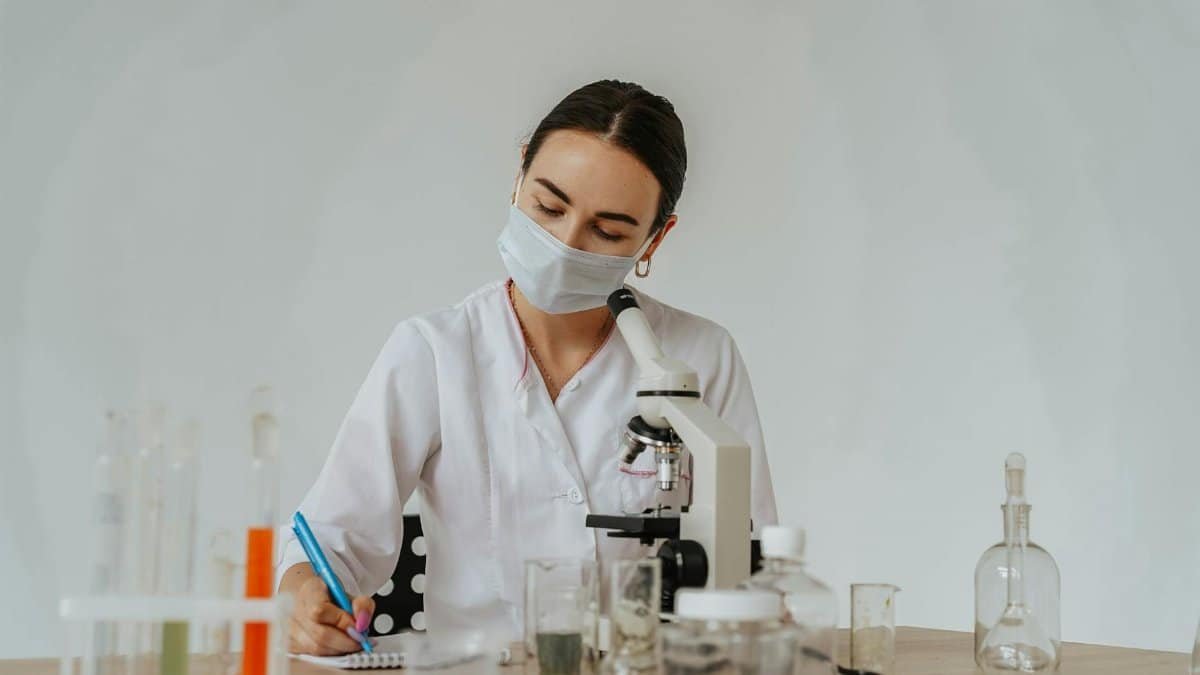 Lab worker analyzing samples with microscope, taking notes. Focus on science and safety.