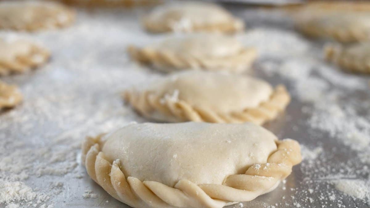 Freshly prepared empanadas on a floured surface, showcasing intricate dough crimping.