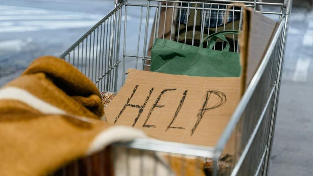 A shopping cart with a cardboard 'Help' sign and belongings, symbolizing urban homelessness.