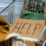 A shopping cart with a cardboard 'Help' sign and belongings, symbolizing urban homelessness.