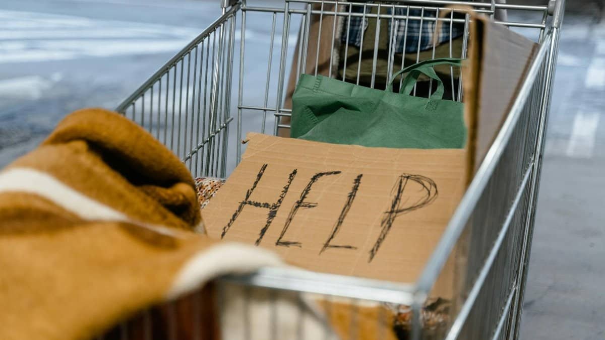 A shopping cart with a cardboard 'Help' sign and belongings, symbolizing urban homelessness.