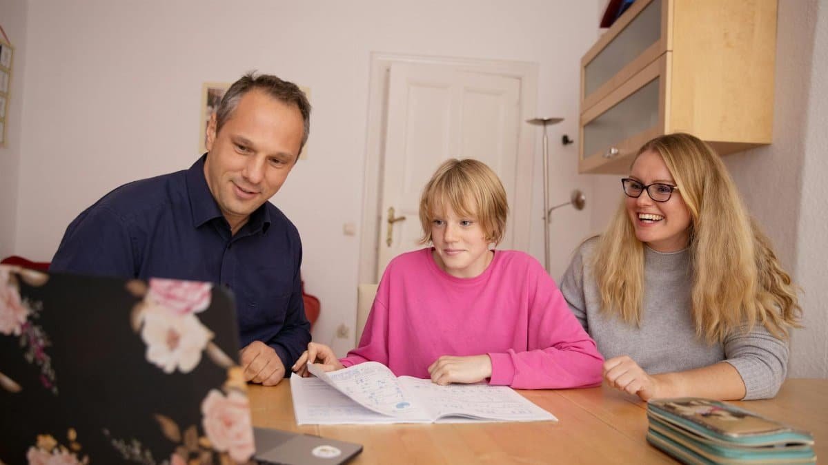 Family engaged in online learning together at home using laptop, focusing on education and connection.