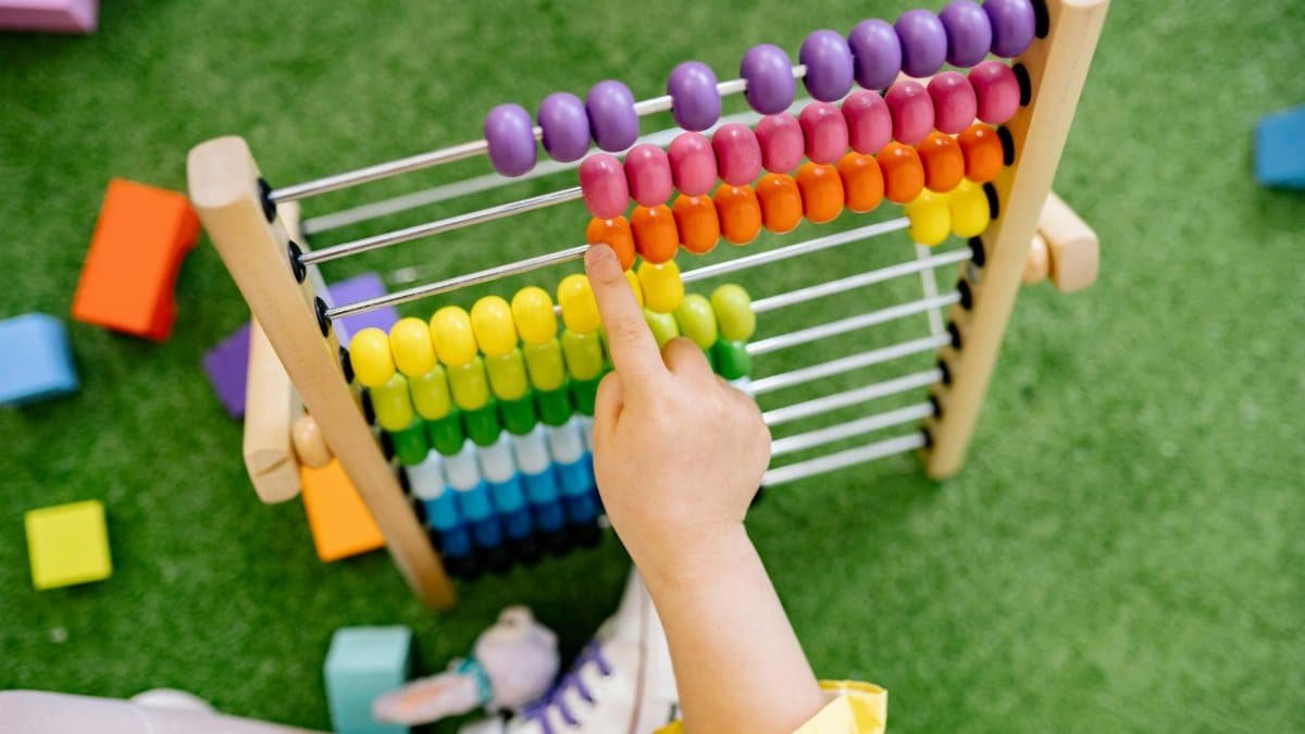 A child's hand using a colorful wooden abacus on green turf, emphasizing playful learning.