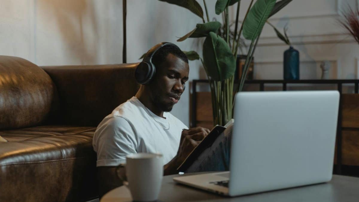 African American man wearing headphones, engaged in online learning at home with a laptop.