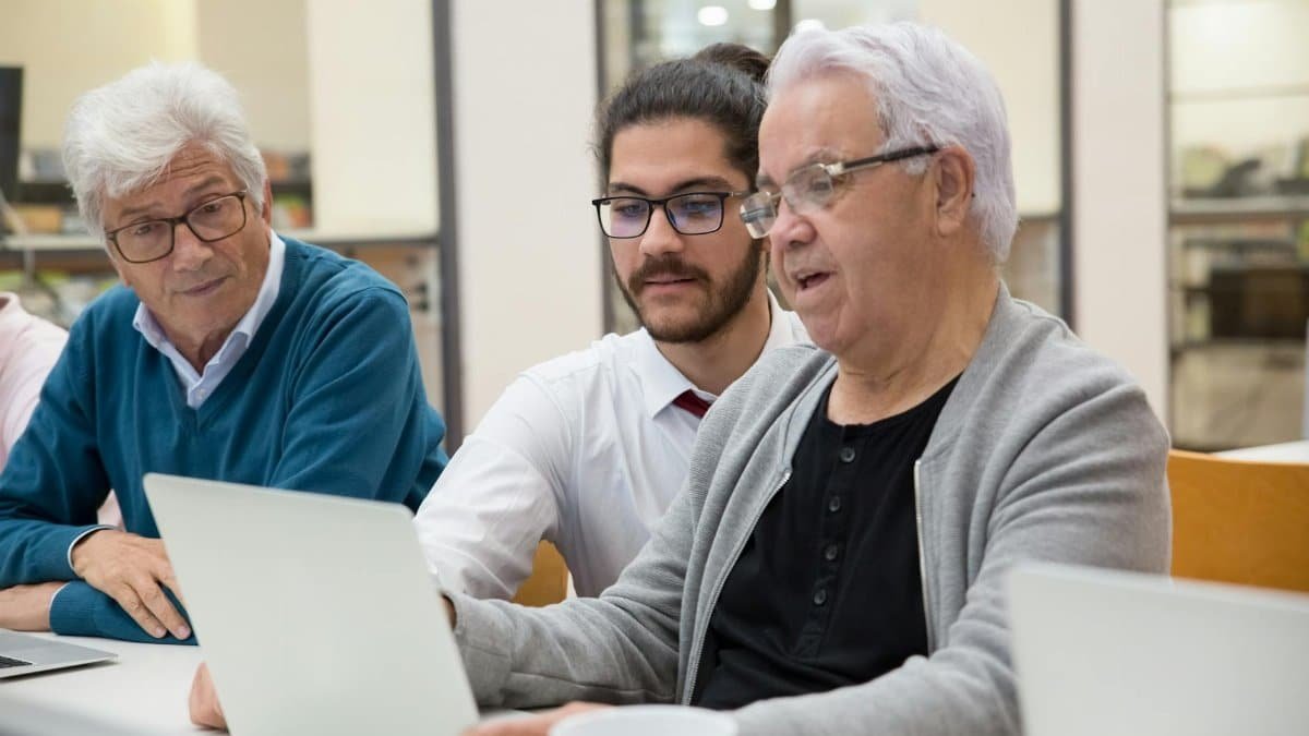 Three men collaborating and learning technology together on laptops indoors.