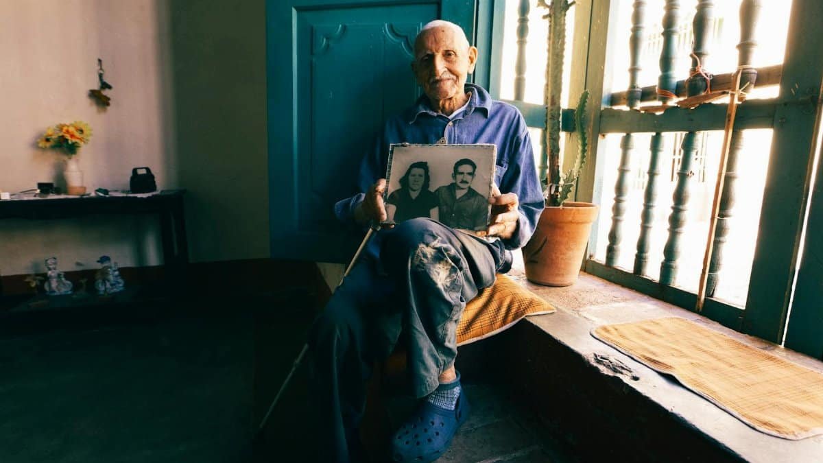 Senior man seated by window, reminiscing with a nostalgic photo.
