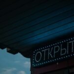 A glowing open sign in Russian under a canopy during nighttime.