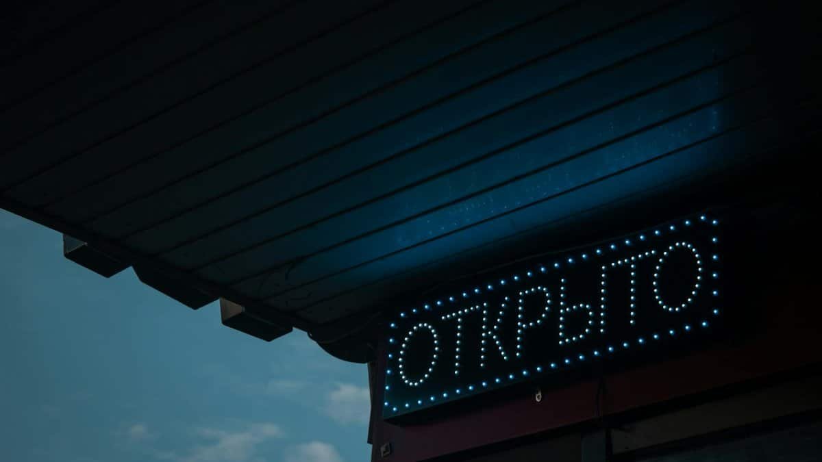 A glowing open sign in Russian under a canopy during nighttime.