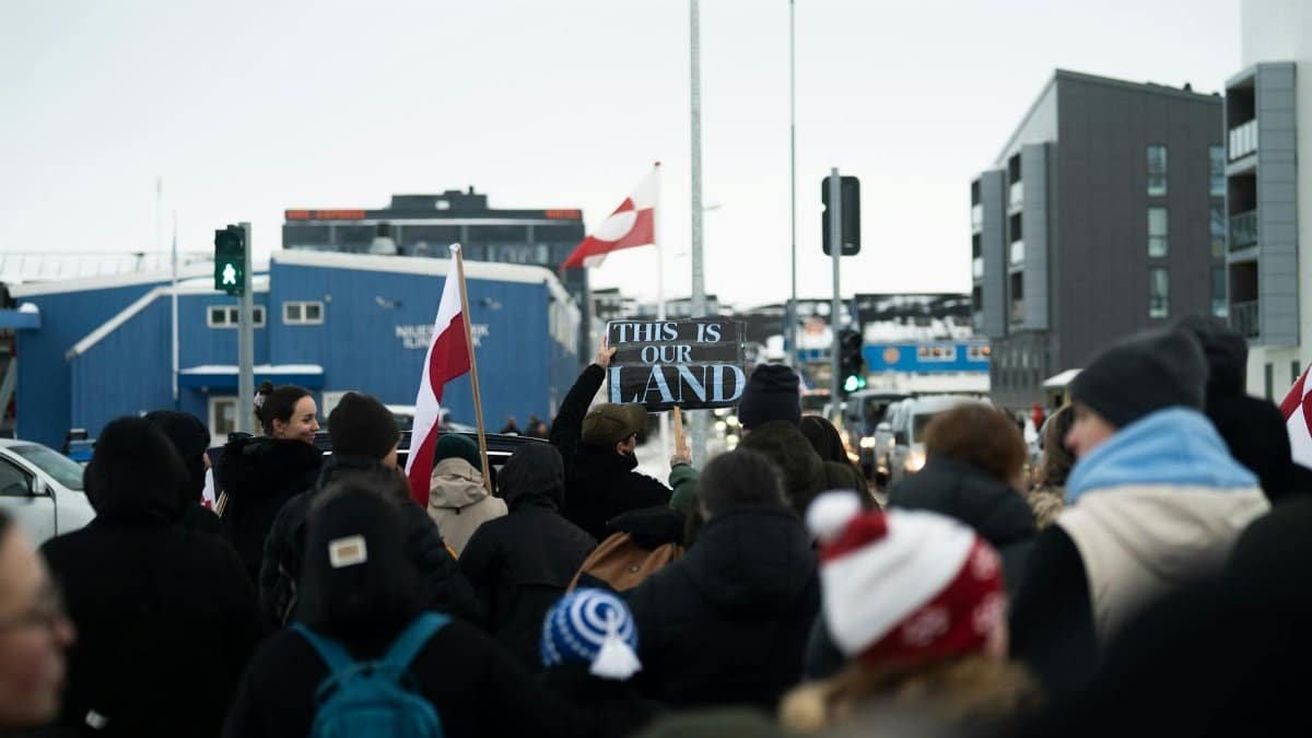 A crowd in Nuuk, Greenland, holds a protest sign reading 'This is Our Land'.