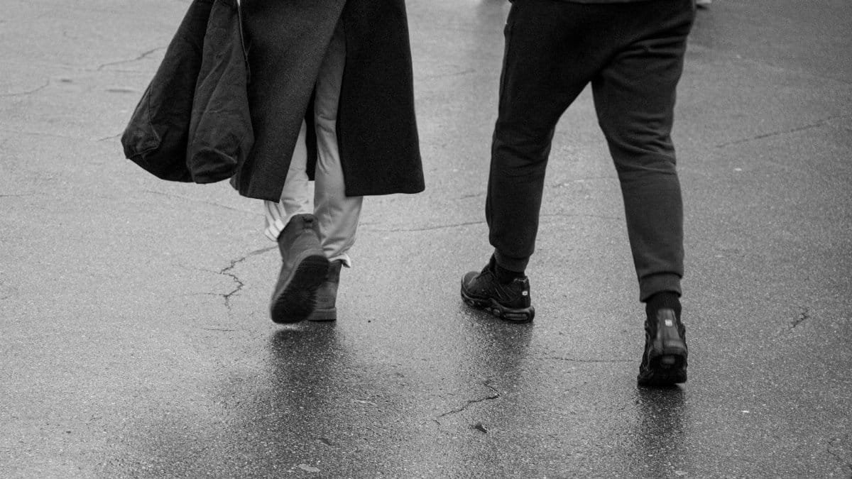 Elegant black and white image capturing a couple walking on a city pavement, showcasing urban life.