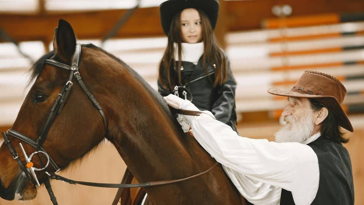 A young girl receives horseback riding lessons from an instructor indoors.